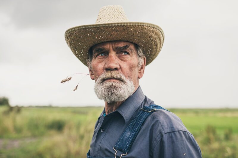 Older white man farmer with whicker hat and wheat stem in mouth