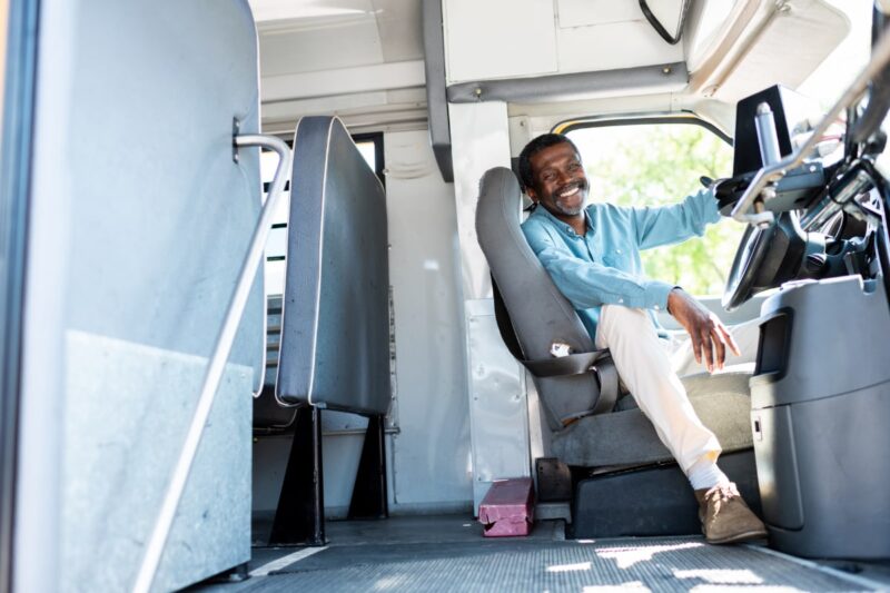 Black man bus driver sitting in seat and smiling at camera